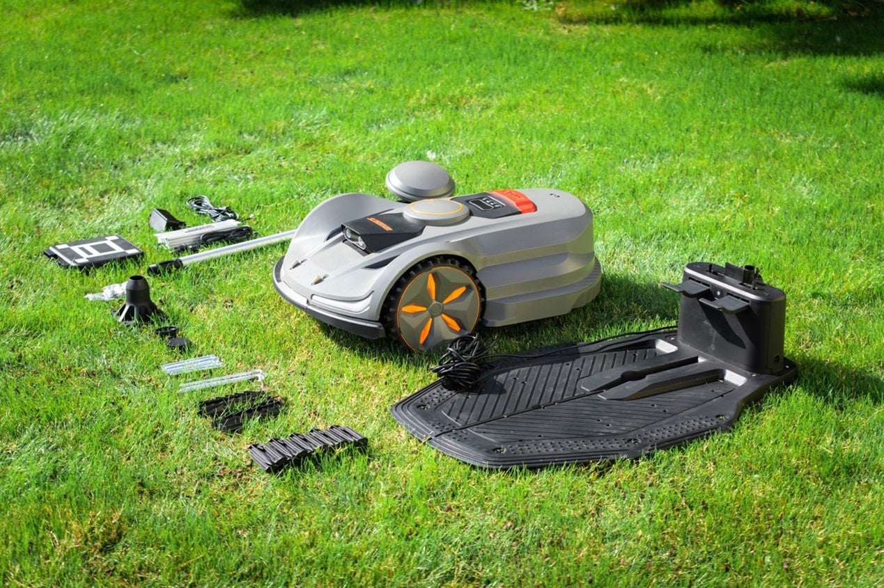 Robotic lawn mower and accessories neatly laid out on green grass, including charging station, cables, and boundary wire components, ready for setup