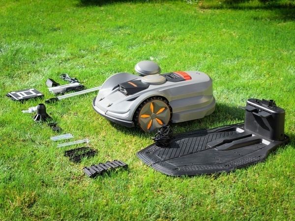 Robotic lawn mower and accessories neatly laid out on green grass, including charging station, cables, and boundary wire components, ready for setup